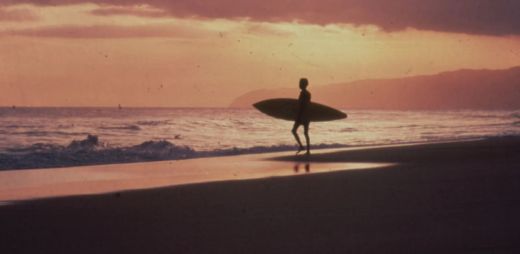 Silhouette of a person holding a surfboard on a beach at sunset.